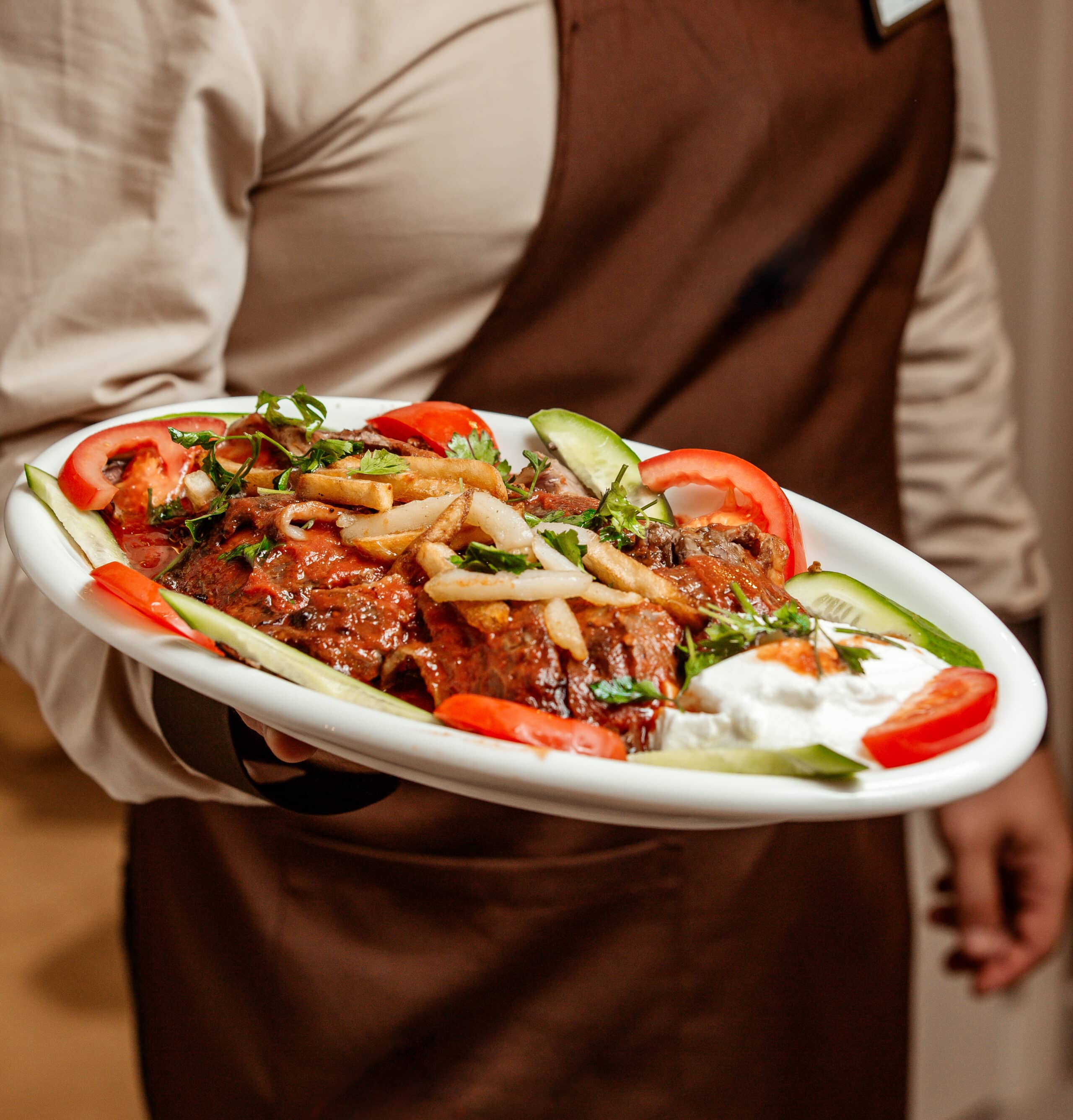 waiter holding a platter of iskender kebab served with yoghurt and vegetable slices
