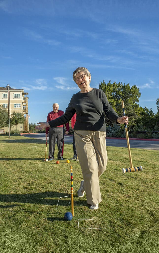 Senior woman laughing and having fun playing croquet at senior living community