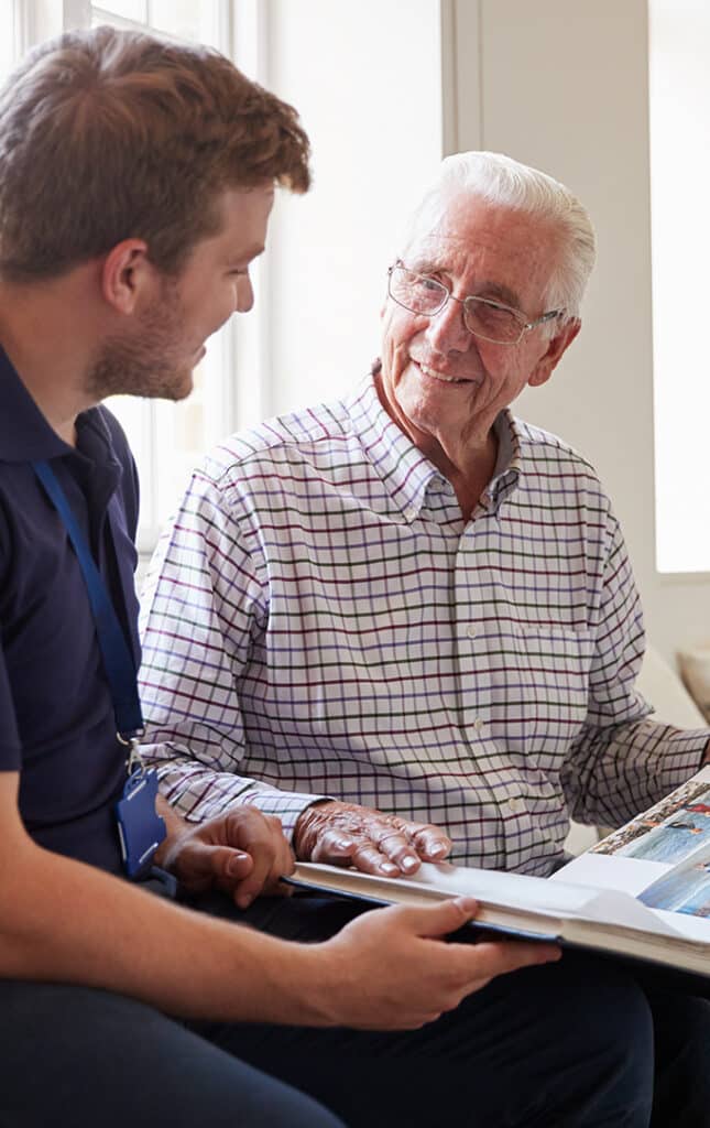 Senior man sitting looking at photo album with male nurse