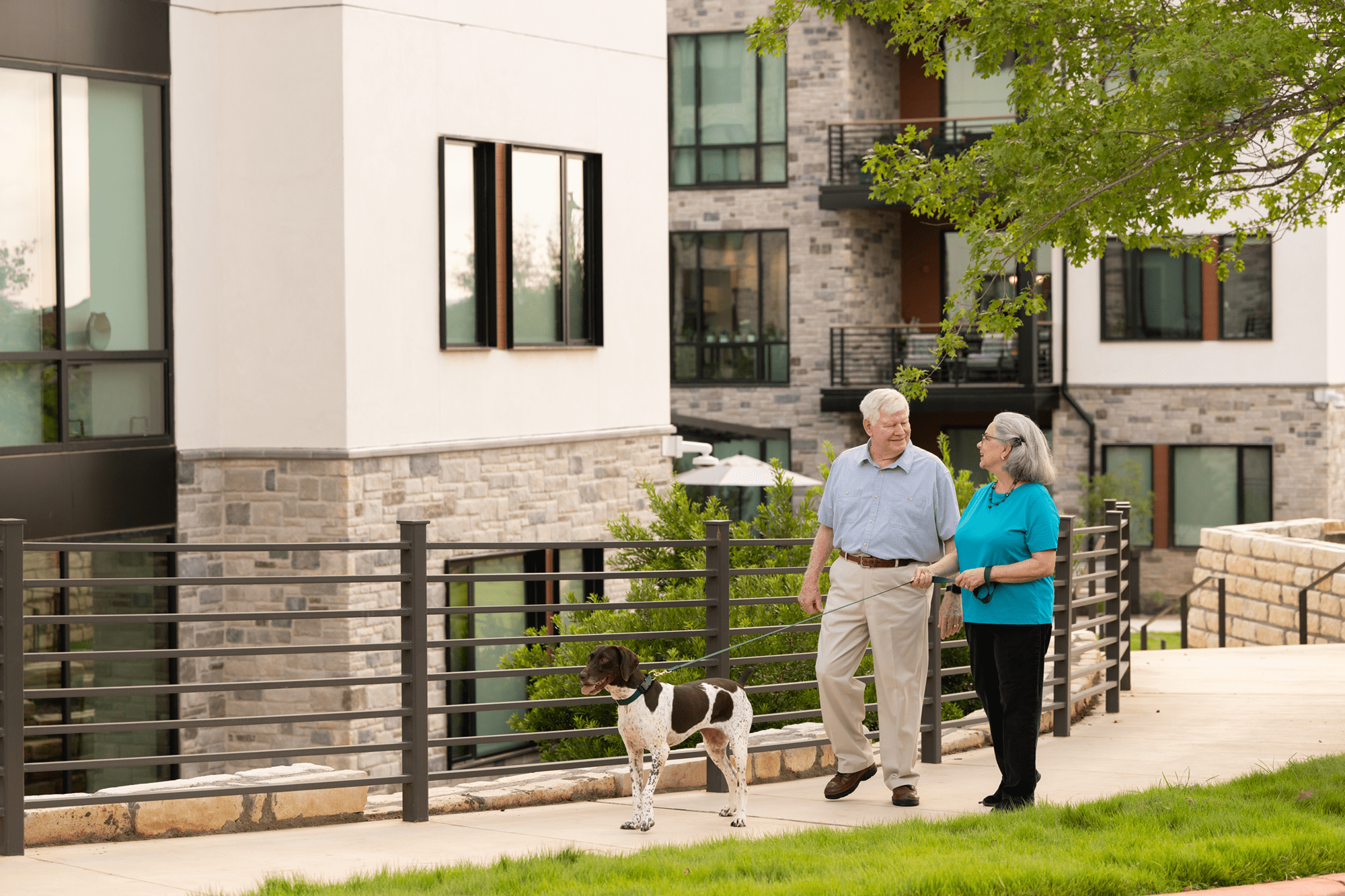 Two elderly people smiling at each other as they walk their dog within a community