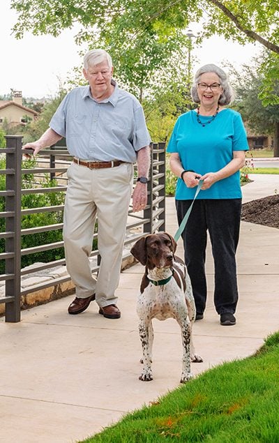elderly couple walking their dog through a park