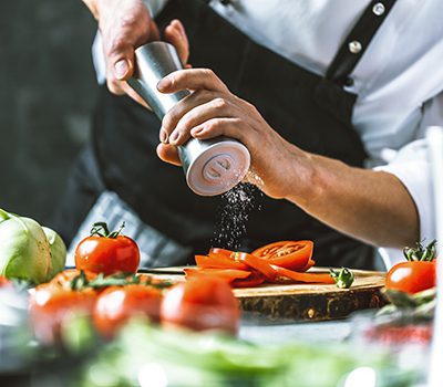 chef sprinkling salt over a cooked meal
