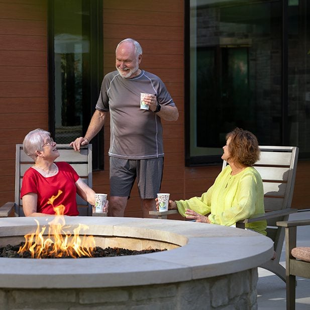 group of seniors enjoying a cup of coffee near an outdoor fire pit.