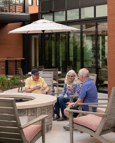a group of residents chatting underneath an umbrella on the outdoor patio