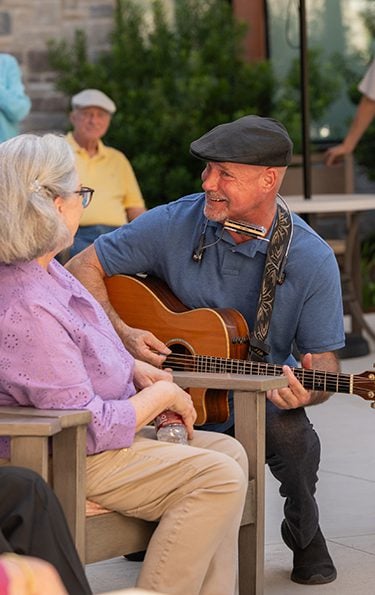 senior man serenading a woman in the outdoor campus at Longhorn Village