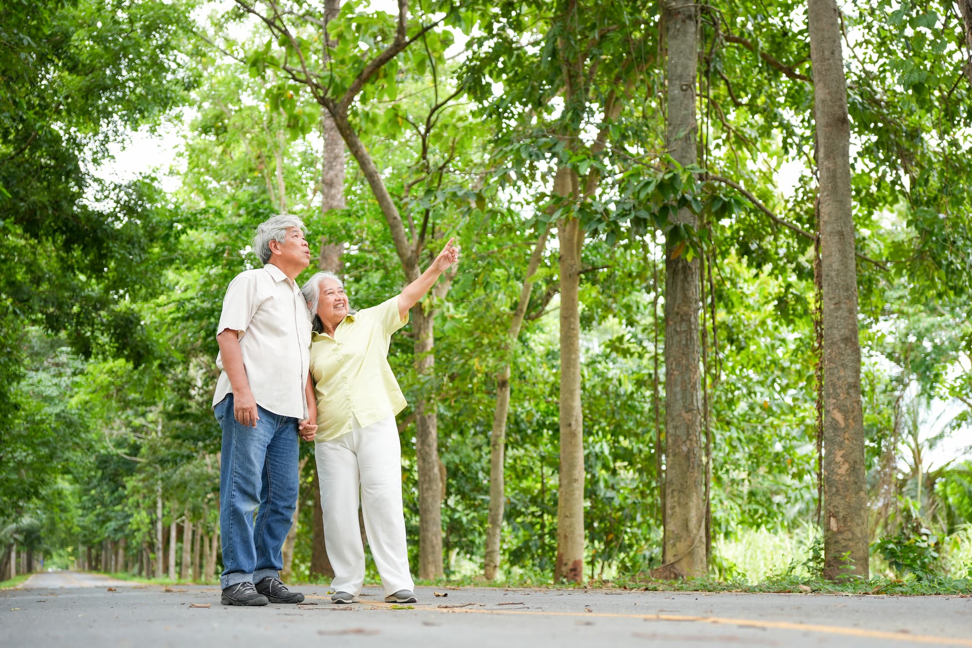 Two senior couples smiling as they stand on one of Austin's best trail paved path, one of them pointing to the treeline