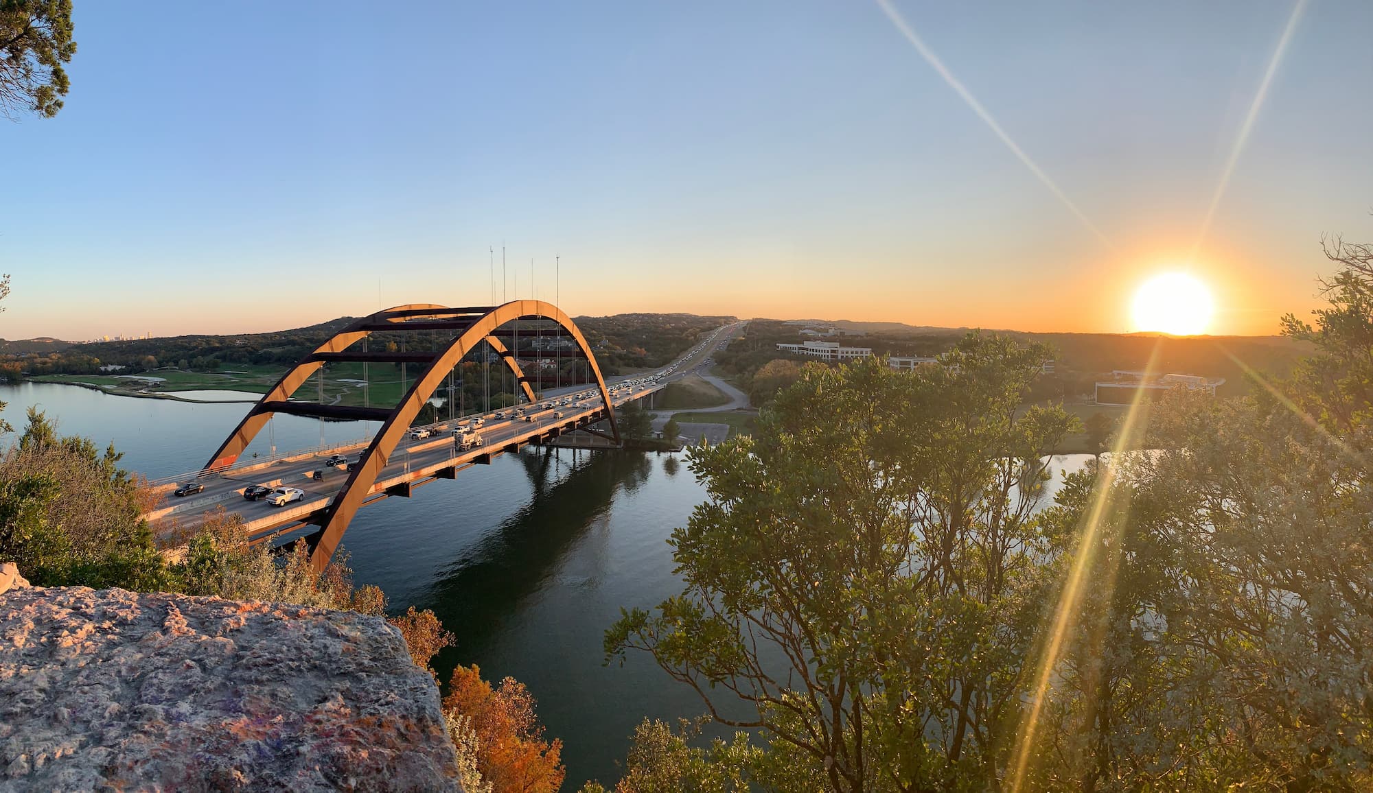 Photo of downtown Austin pedestrian and car bridge spanning over a running river in the forest.