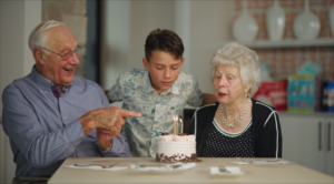grandson celebrates with his grandparents for their birthday while they blow out a candle