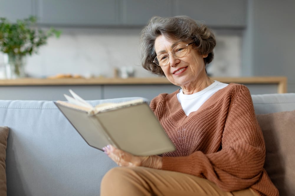 senior woman reads a book on the couch in her residence.